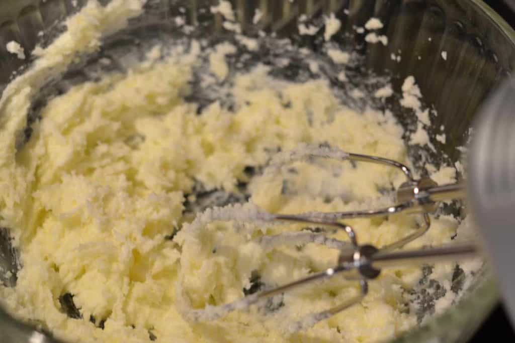 Hand mixer whisks in a bowl of butter and sugar that have been combined