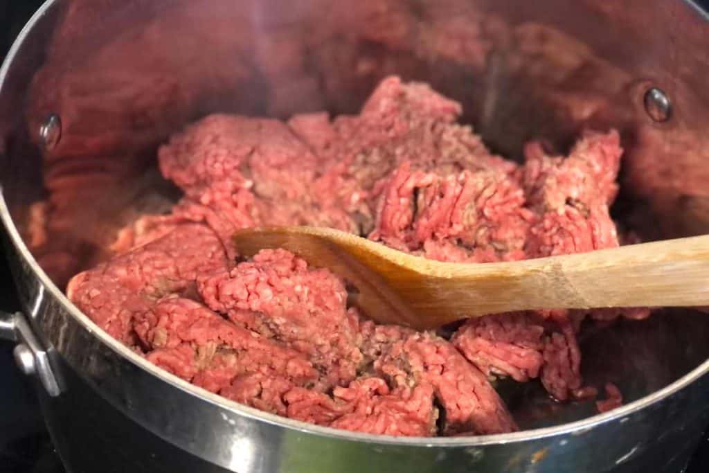 Raw ground beef in a pot on the stove beginning to brown