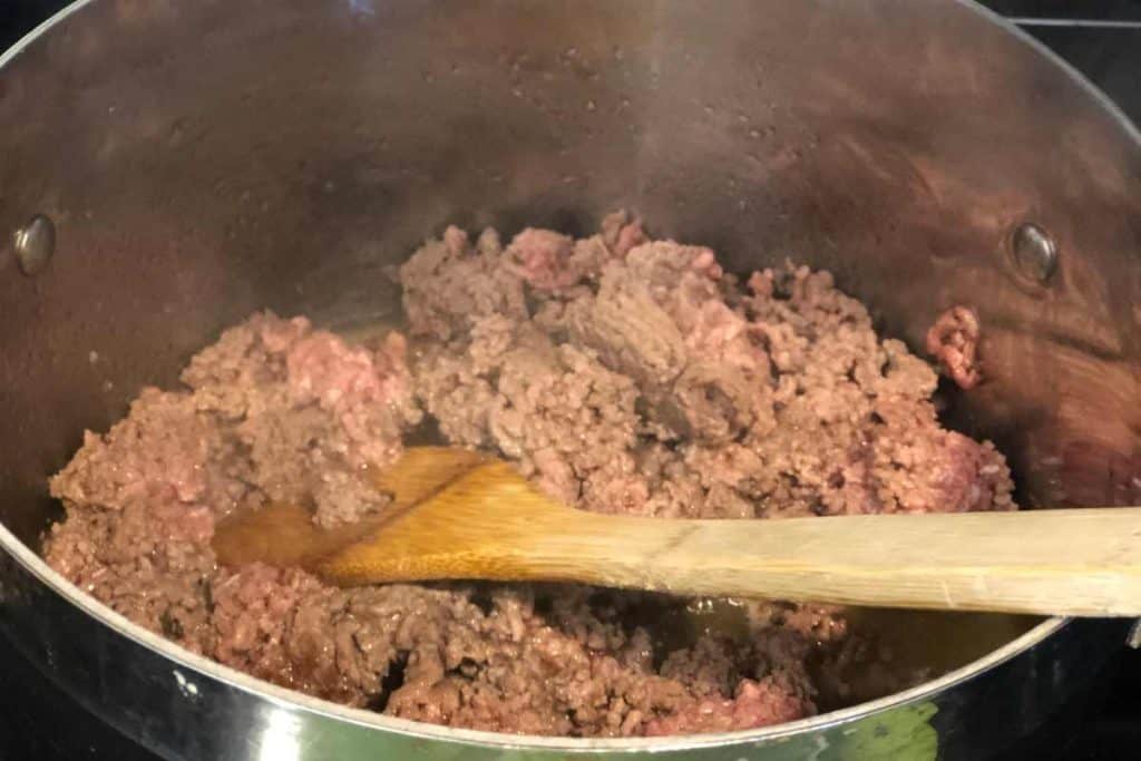 Ground beef cooking on the stove in a pot with a wooden spoon