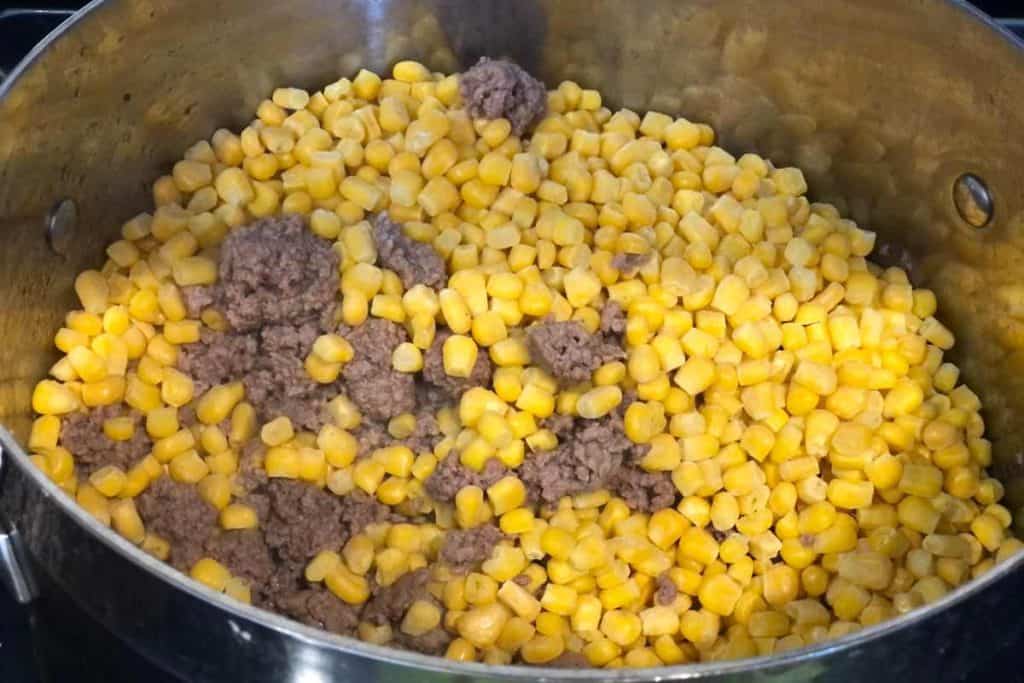 Frozen corn added to the ground beef mixture in a pot