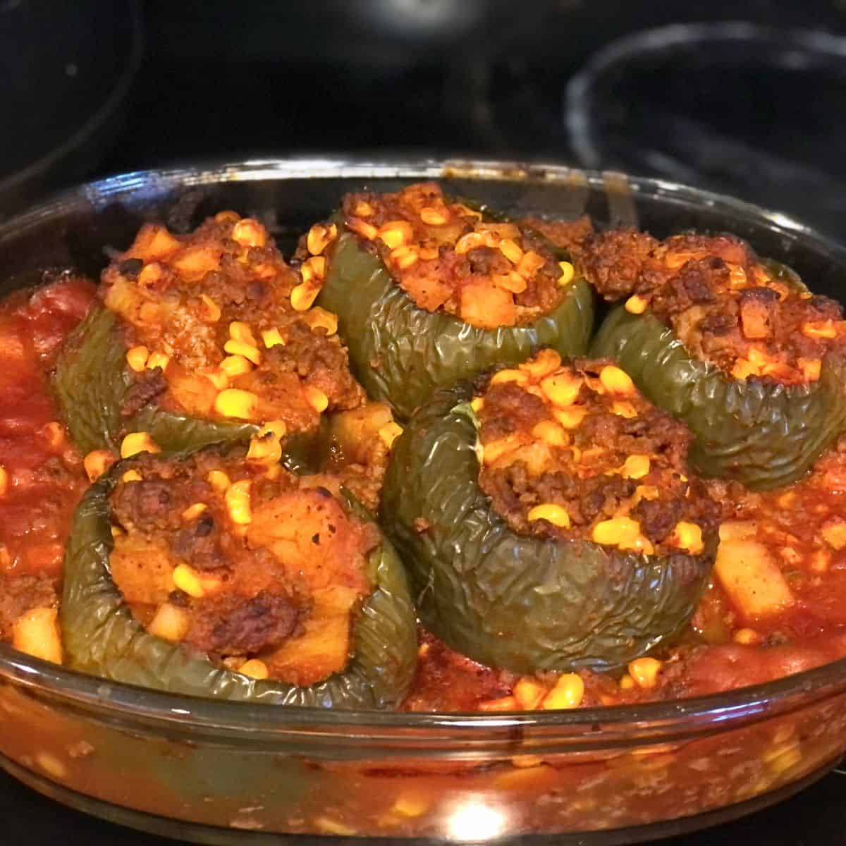 Stuffed peppers that have been cooked in the oven and are now ready to eat with corn, tomato sauce, green bell peppers and ground beef