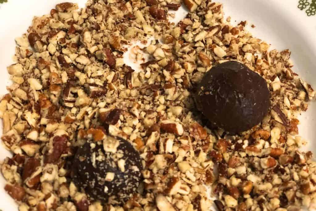 Raw chocolate truffles in a bowl of chopped pecans being rolled around to get coated in chopped pecans