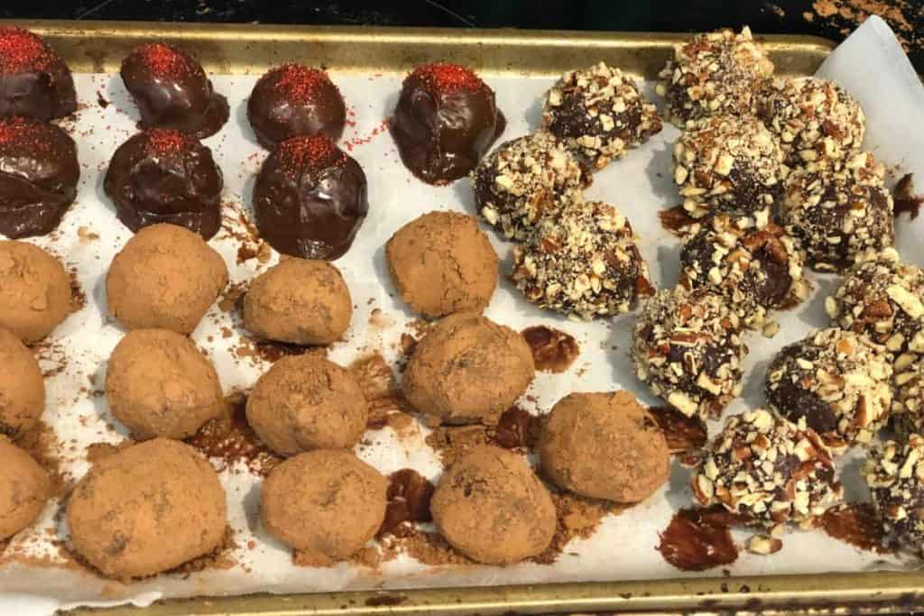 Parchment paper lined baking sheet with finished truffles that are coated in chocolate, cocoa powder and pecans on a try to firm up.