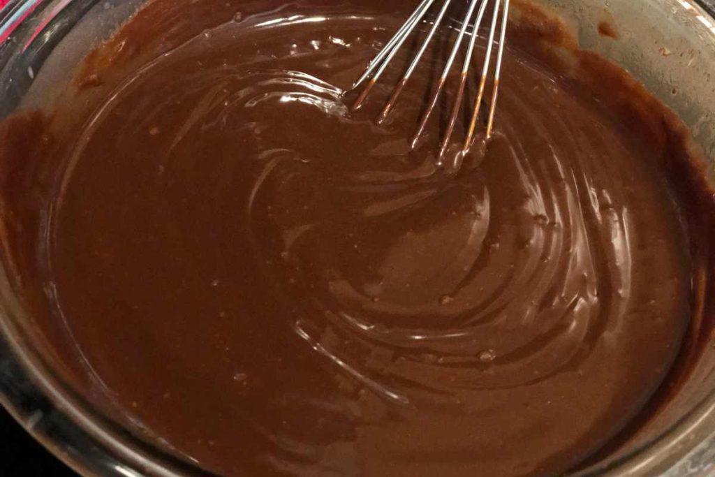 Melted chocolate in a bowl in it with a whisk in the bowl.