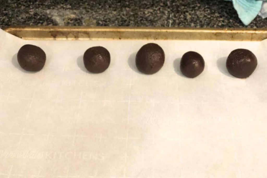 Five chocolate truffles on parchment paper after being formed from the chilled mixture.