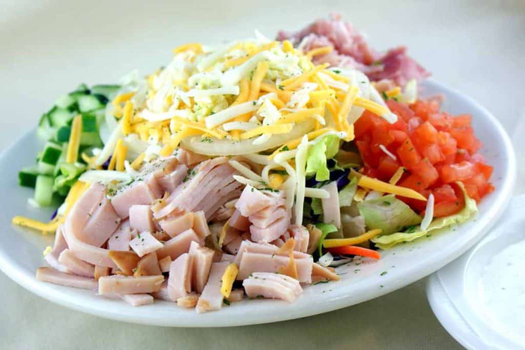 A chef salad with cheese, tomatoes, ham, turkey, cucumbers and lettuce.