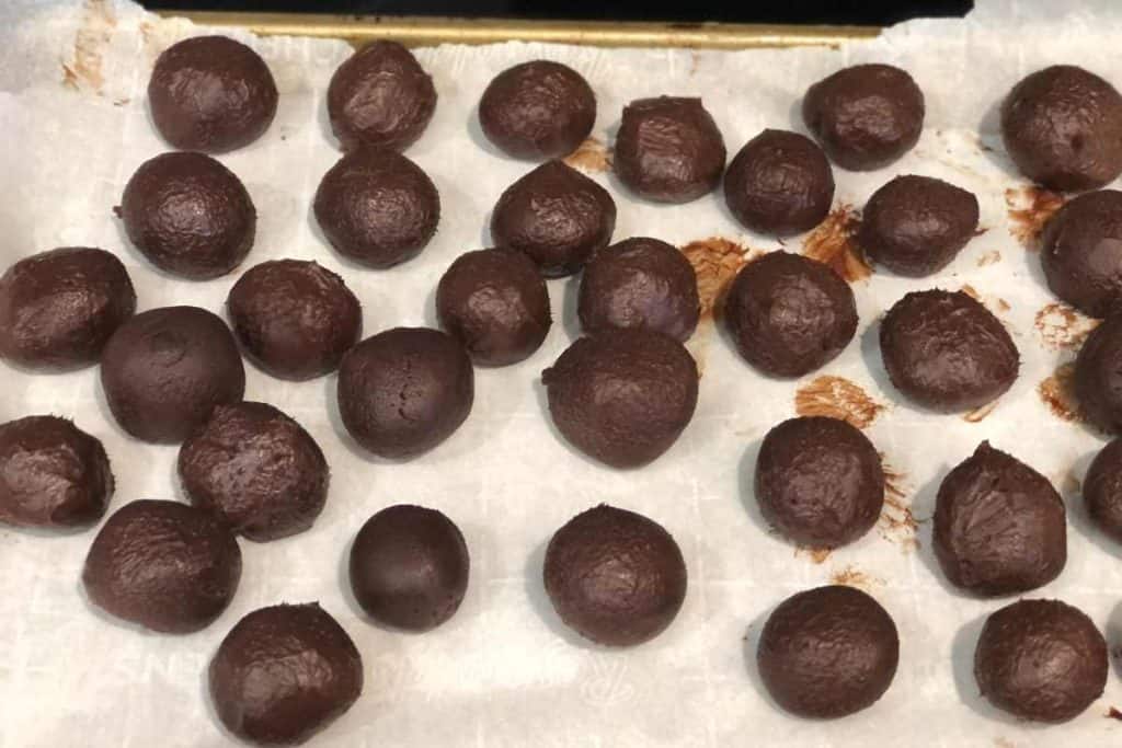 Raw chocolate truffles rolled into balls on a parchment lined baking sheet after they have been shaped.