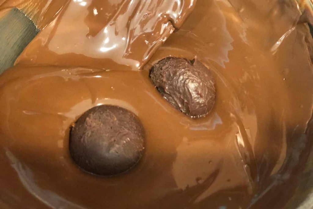Raw truffles in a bowl of melted chocolate to be coated in melted chocolate.