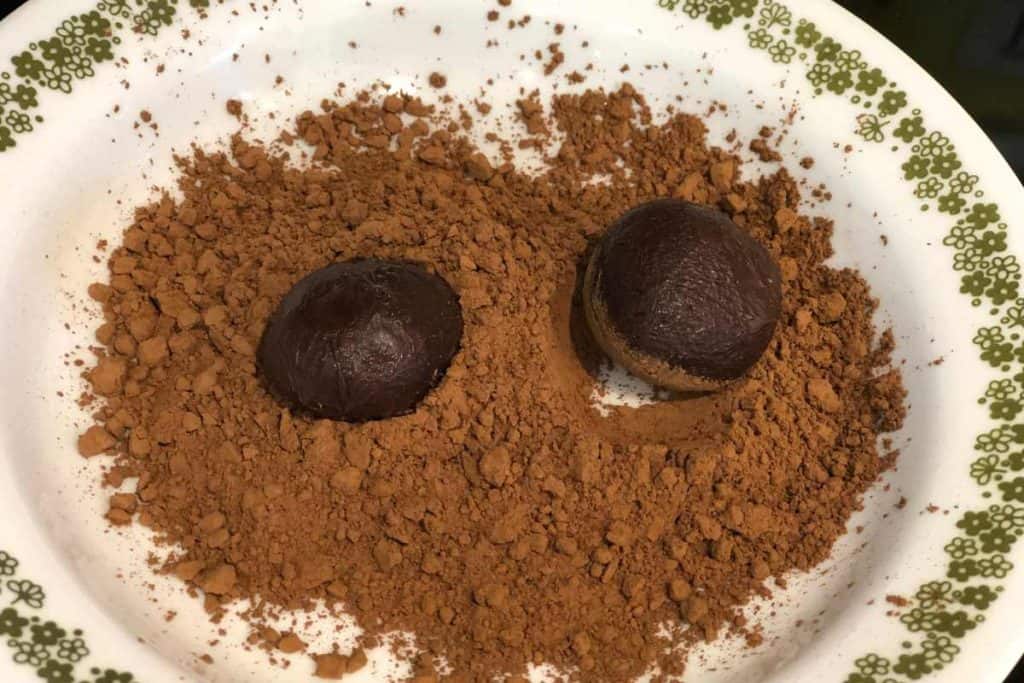 Raw chocolate truffles in a bowl of dry cocoa powder and being rolled around in cocoa powder for topping
