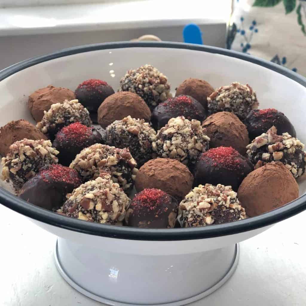 White cake tray holding multiple truffles topped with sugar sprinkles, pecans and cocoa powder