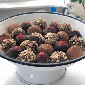 White cake tray holding multiple truffles topped with sugar sprinkles, pecans and cocoa powder