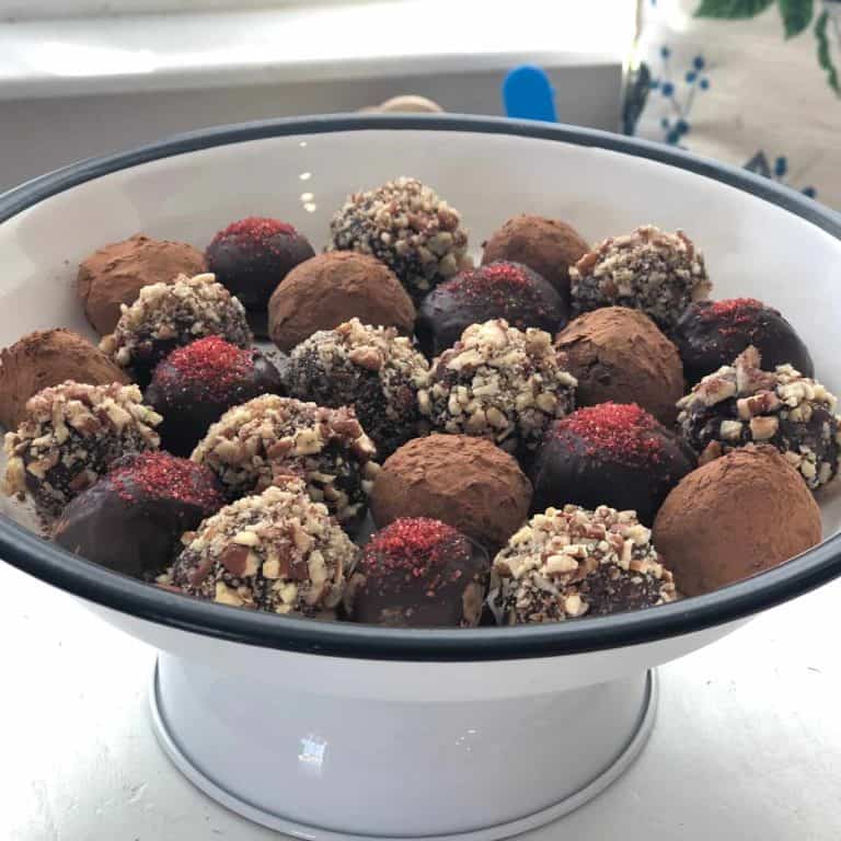 White cake tray holding multiple truffles topped with sugar sprinkles, pecans and cocoa powder