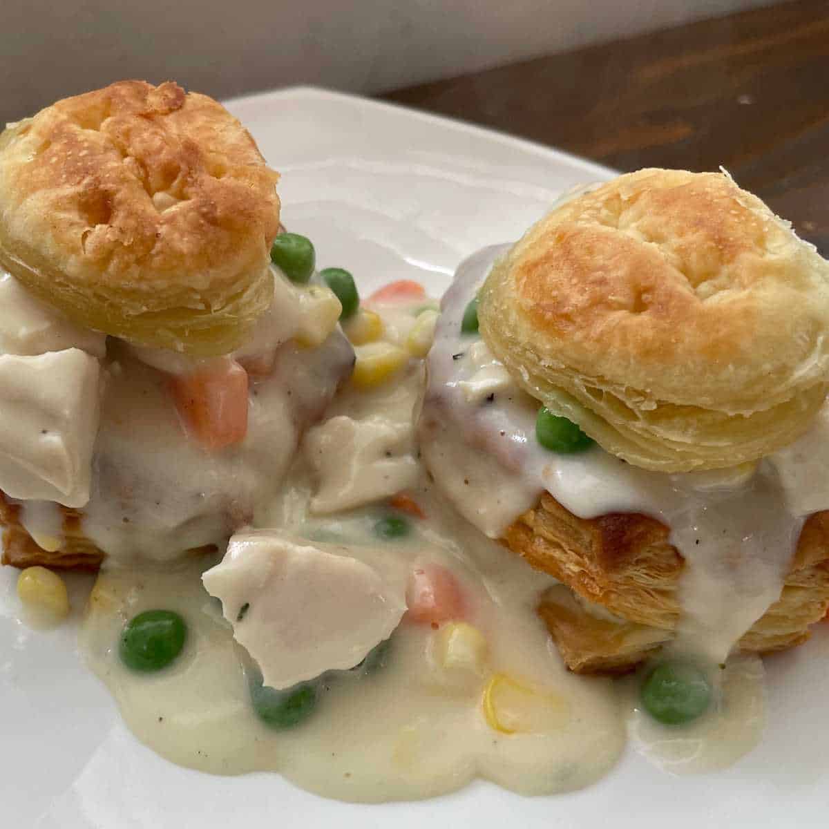 Easy Chicken Pot Pie recipe completed and on a white plate. The pot pie filling is poured into pastry puff shells with the lids of the puff pastry on top.