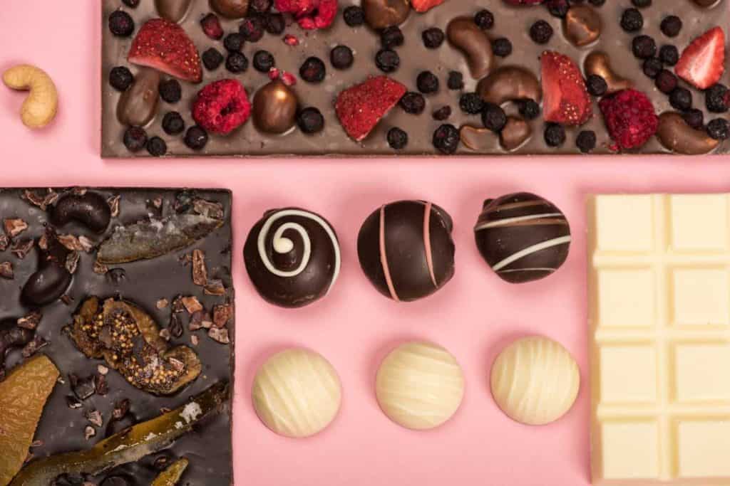 Lots of chocolates including some chocolate bark with strawberries and fruits along with a white chocolate bar and chocolate truffles