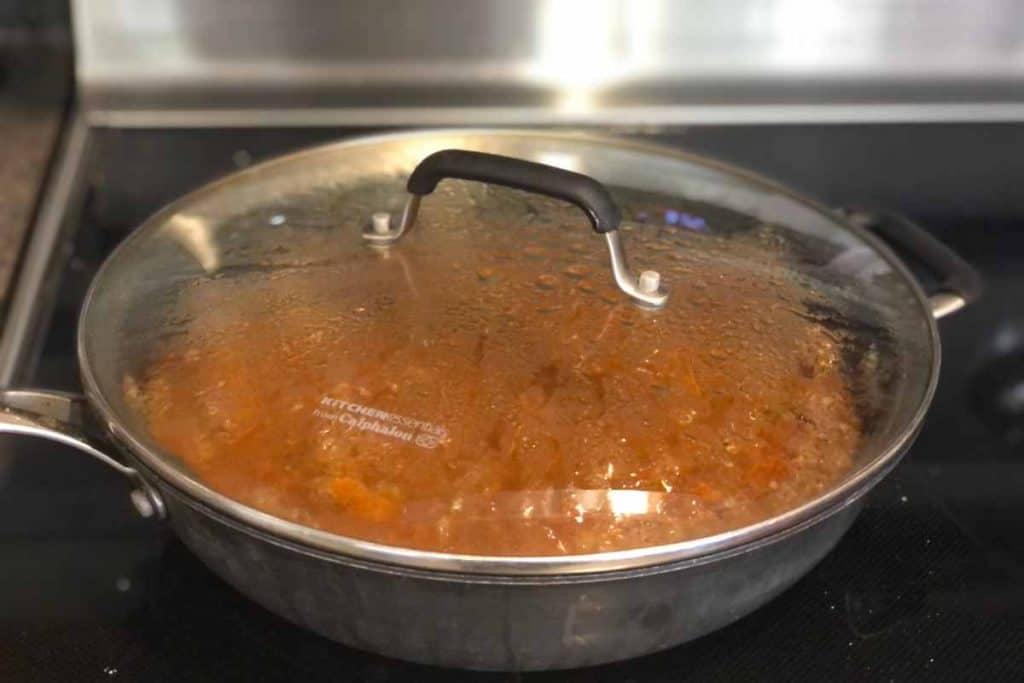 Skillet with sloppy joes cooking with a lid on the pot, still on heat on the stove.