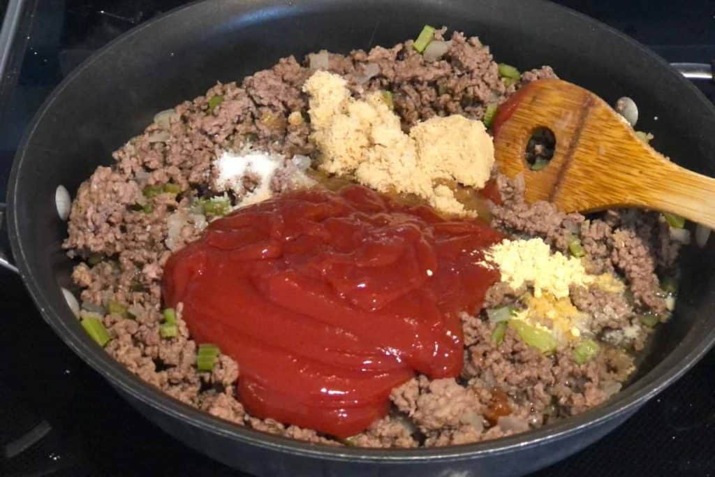 Ingredients for Sloppy Joes sauce poured over cooked ground beef, ready to be stirred together to make sauce.