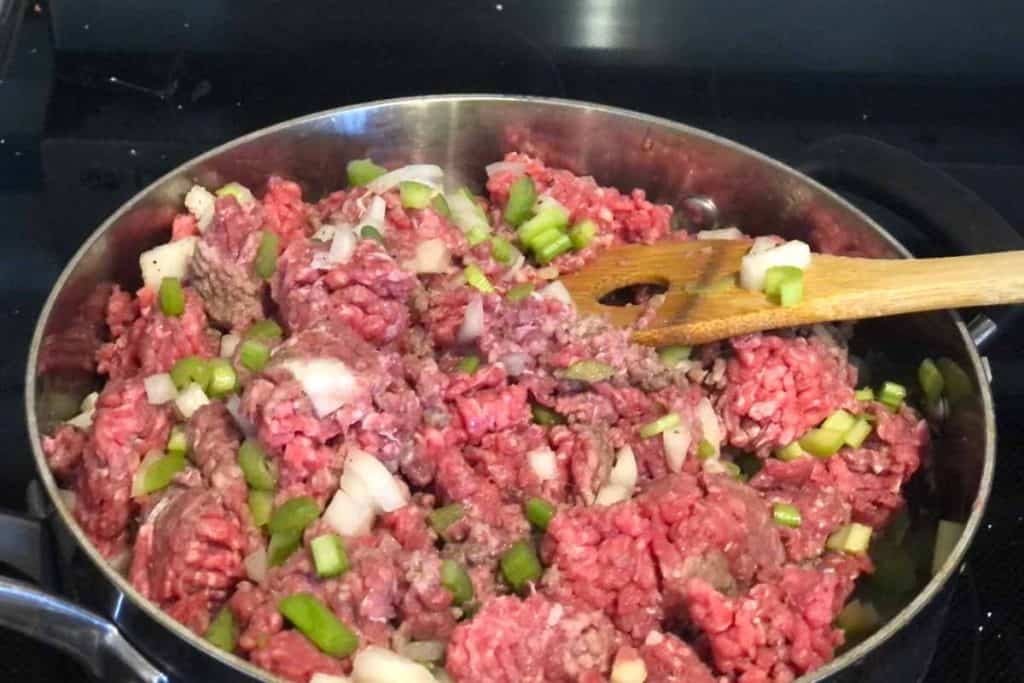 Raw ground beef cooking in a skillet with chopped up celery and onions.