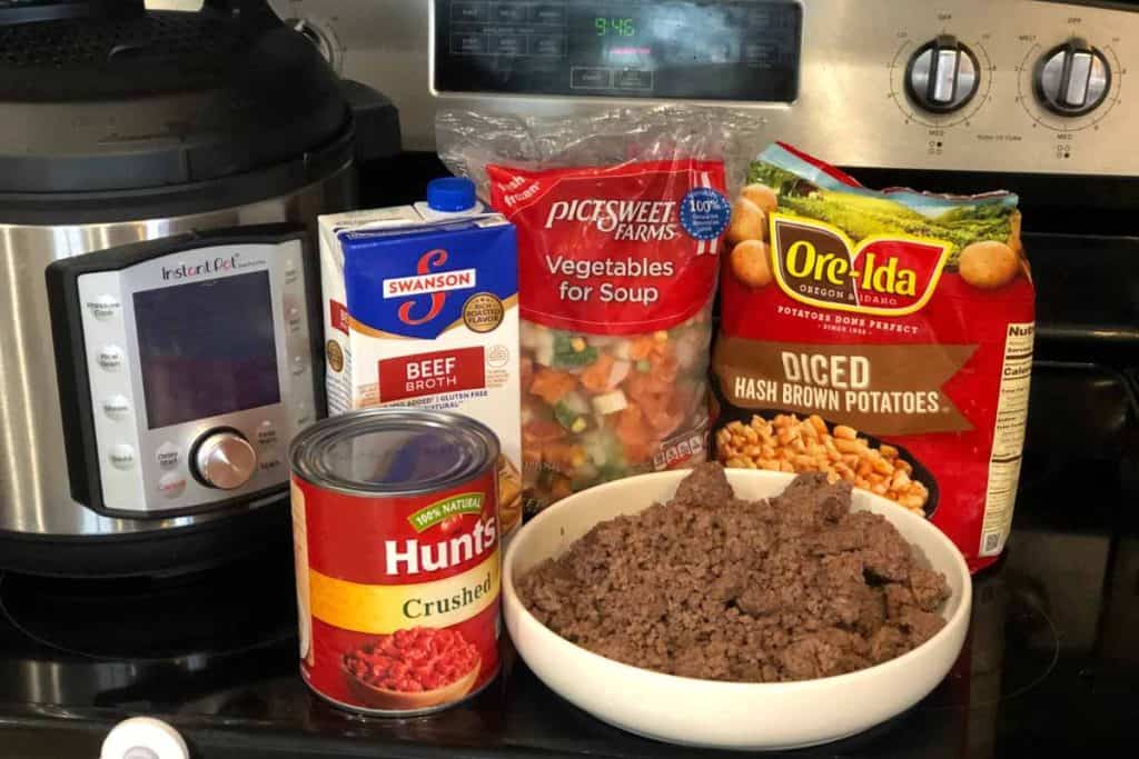 Ingredients for Easy and Quick Instant Pot Vegetable Beef Soup Recipe including frozen hash brown potatoes, a bag of frozen mixed vegetables, a carton of beef broth, a can of crushed tomatoes and cooked ground beef, along with an instant pot