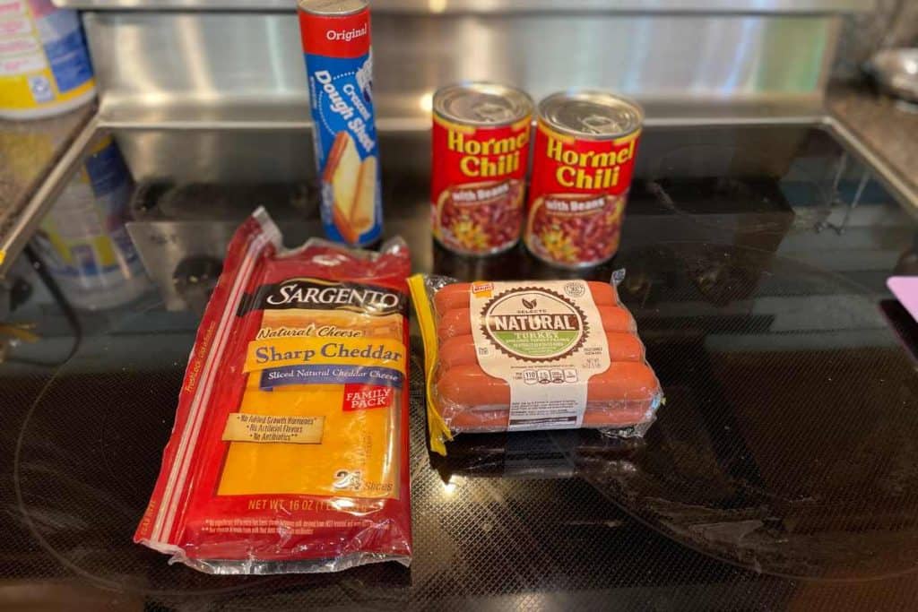 Ingredients for Chili Dog Casserole including sliced cheddar, hot dogs, canned chili and crescent roll dough