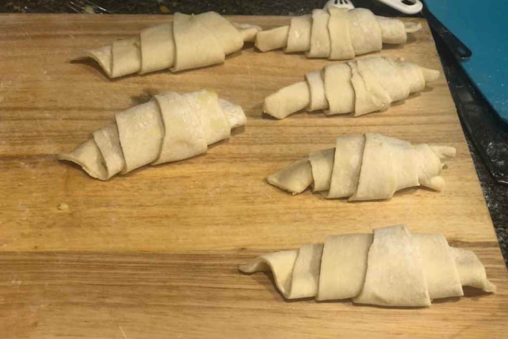 Rolled up almond croissants on a cutting board waiting to be put on a baking sheet