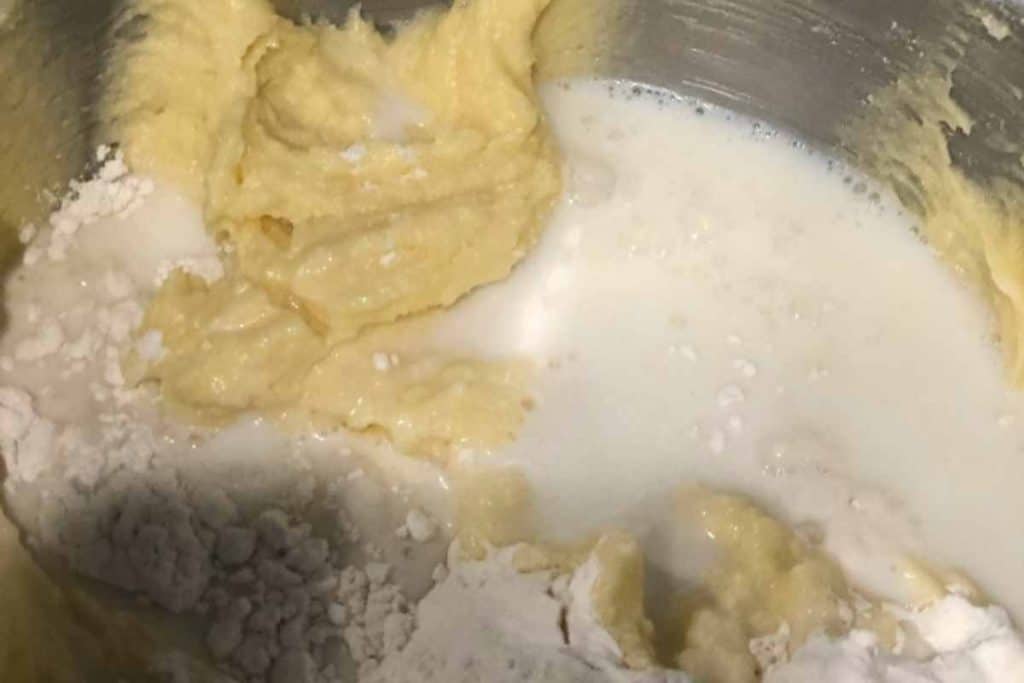 Adding milk and flour to the lemon pound cake batter in the mixing bowl of the electric mixer.