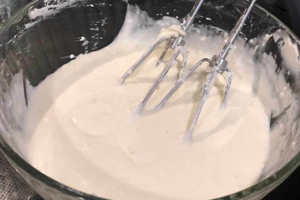 Cream cheese mixed with lemonade concentrate in a large glass bowl with the beaters of an electric mixer