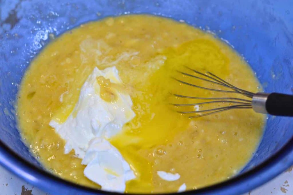 Melted butter and yogurt sitting on top of banana bread batter ready to be mixed together with a wire whisk