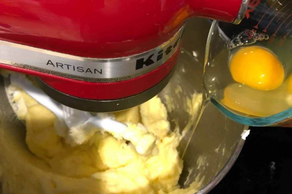 Adding eggs into a kitchenaid mixer bowl filled with cake batter for the Easy Southern Lemon Pound Cake recipe