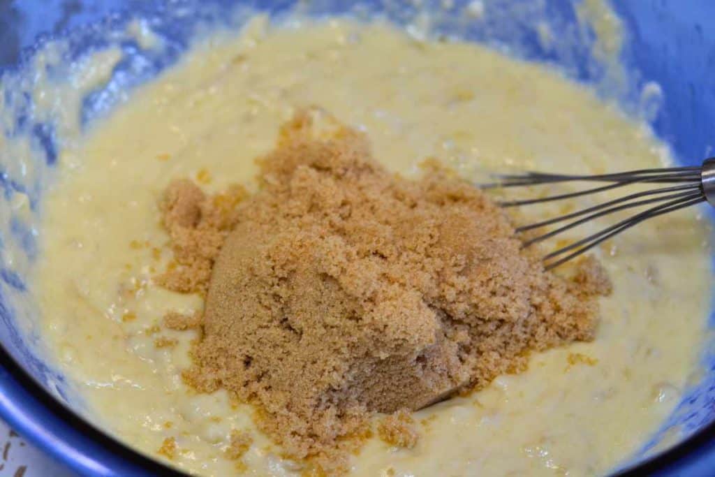 Brown sugar being added to banana bread batter that needs to be mixed in with the wire whisk
