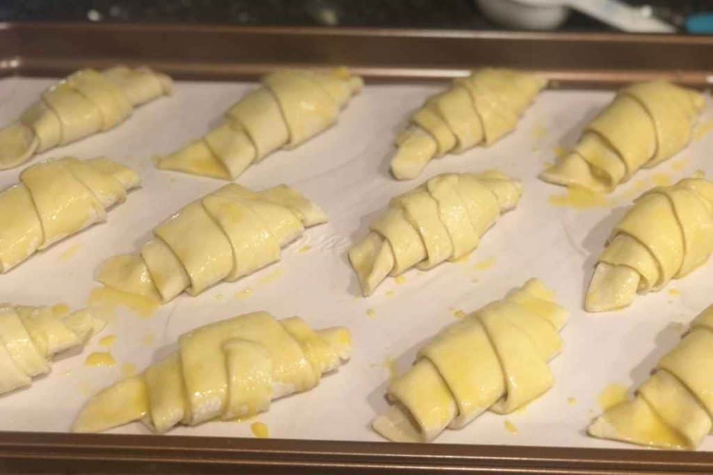 Almond croissants rolled and covered in egg wash and ready to go into the oven