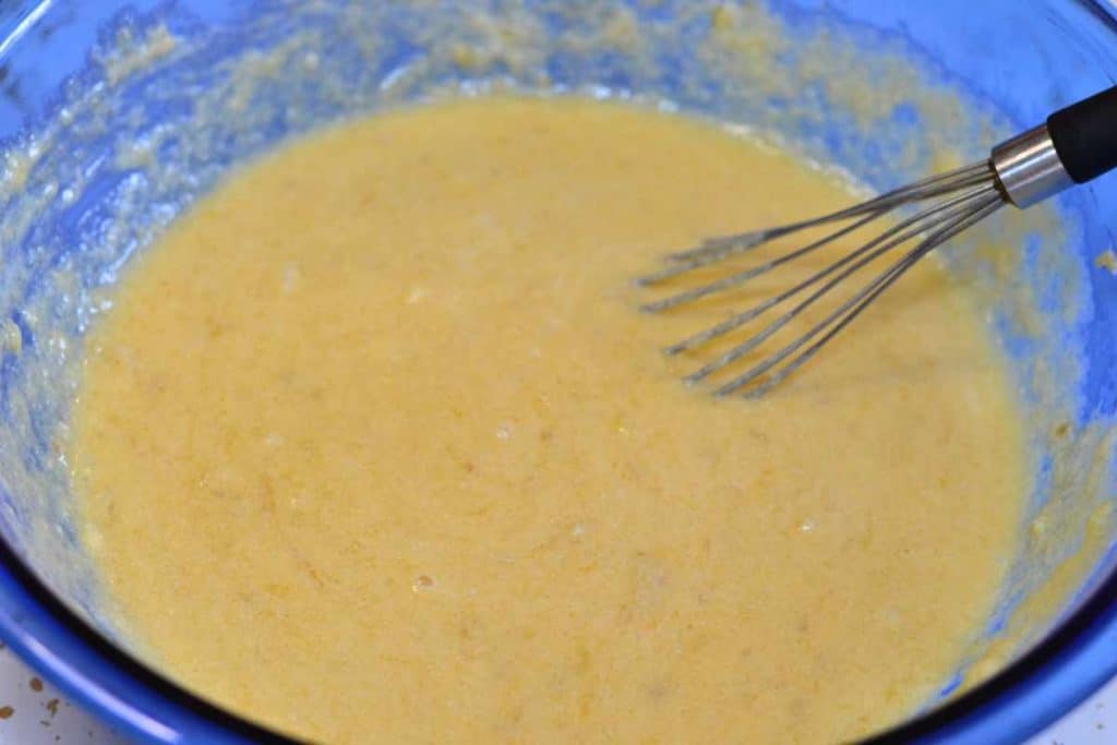 Combined wet ingredients for banana bread in a blue mixing bowl with a wire whisk
