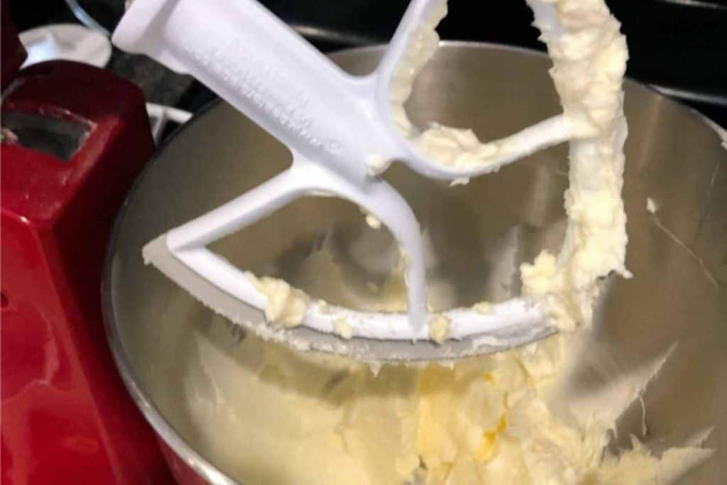 Beater of electric mixer raised above the creamed butter and shortening that have been combined in the mixing bowl