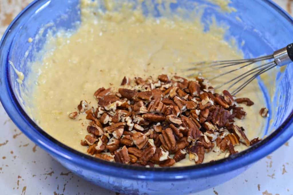 Pecans on top of banana bread batter waiting to be mixed in with a wire whisk
