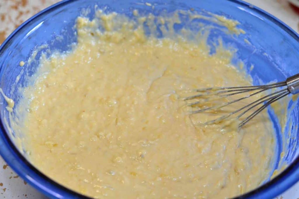 Banana bread batter with a wire whisk in a blue bowl.