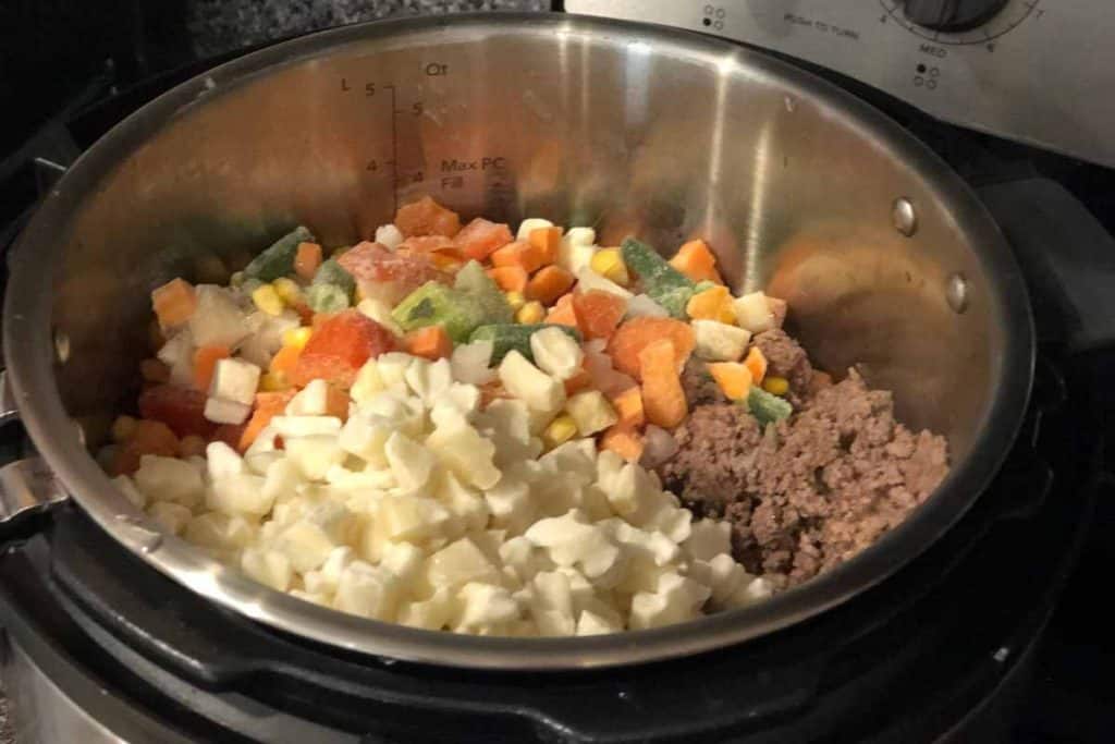 Frozen vegetables and potatoes along with some cooked ground beef in an instant pot as the beginnings of Instant Pot Vegetable Beef Soup Recipe