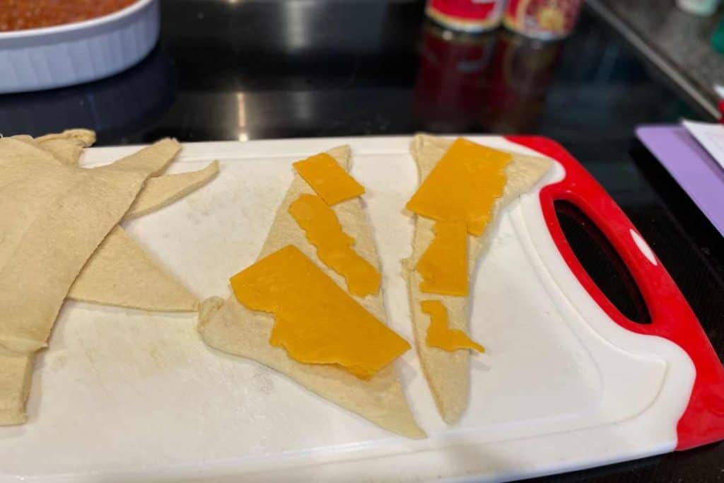 Crescent roll dough layed out in triangles with cheese on top to roll up the hot dogs into the dough.