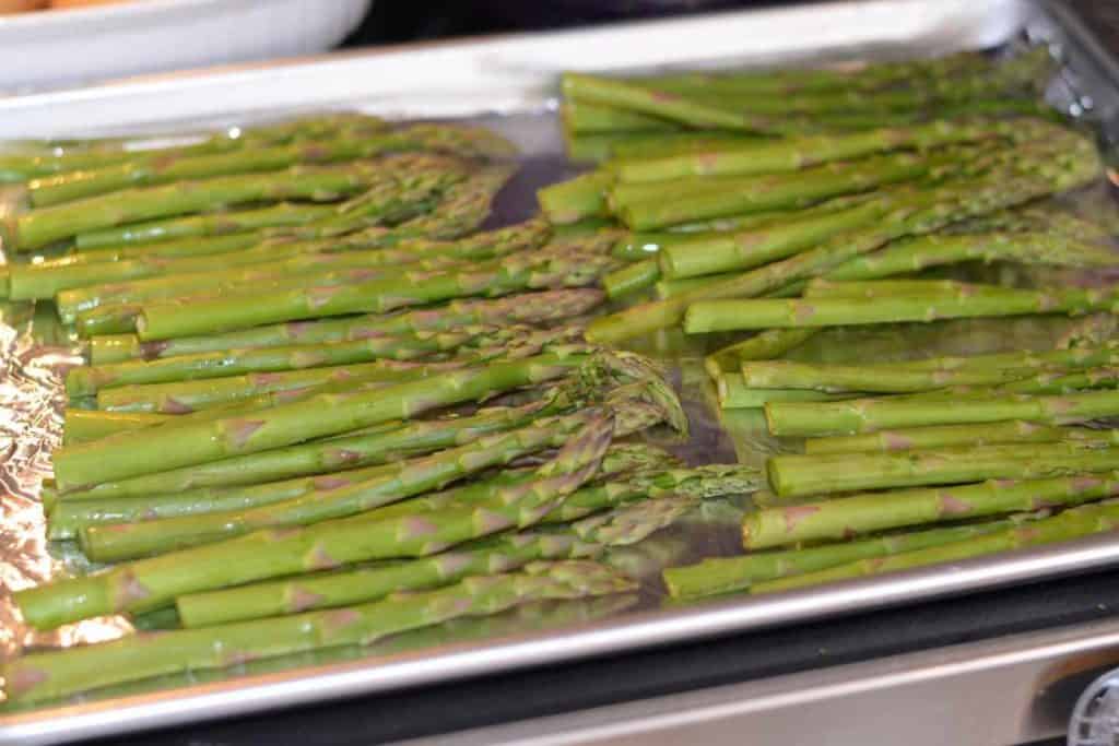 Raw asparagus lined up on an aluminum foil lined baking sheet