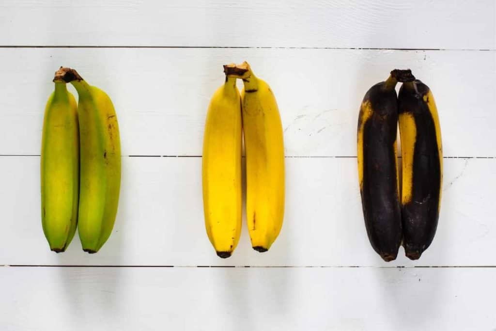 3 sets of bananas at different stages of ripeness including green underripe bananas, perfecly yellow ripe bananas and brown over ripe bananas