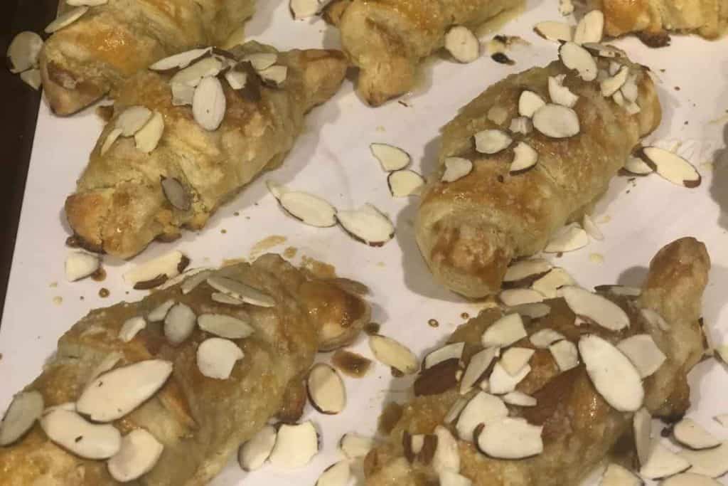 Almond croissants cooked and cooling on a parchment lined baking sheet