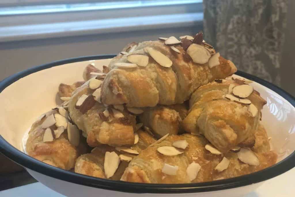 White cake stand holding fresh almond croissants in front of a window