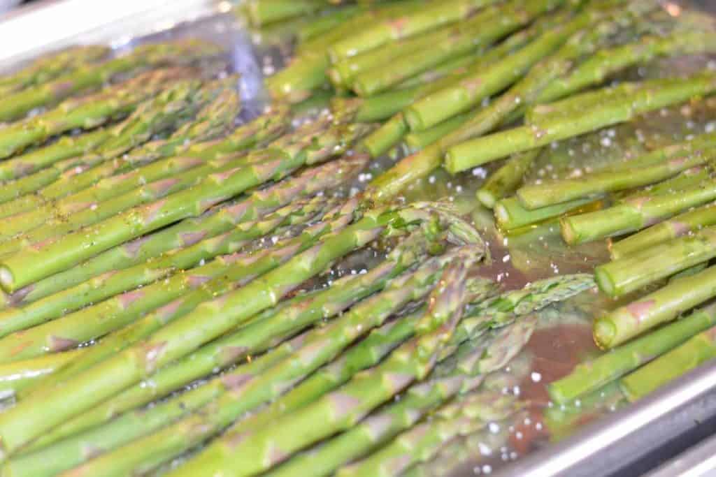 Close up of raw asparagus with salt and pepper on an aluminum foil lined baking sheet