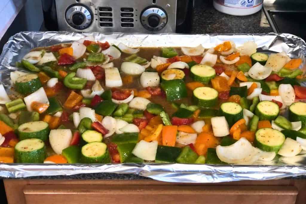 Raw vegetables layed out on a lined cookie sheet with salt and pepper and Italian dressing poured over the baking sheet