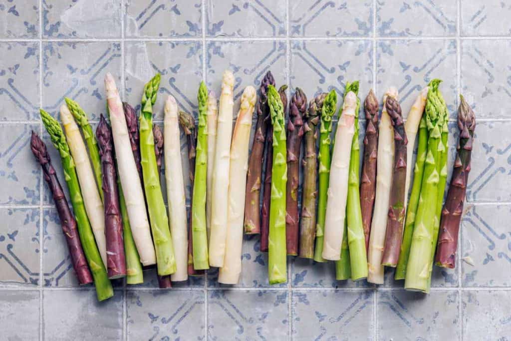 Green, purple and white asparagus all mixed together and lined up on a Spanish blue and white tile countertop
