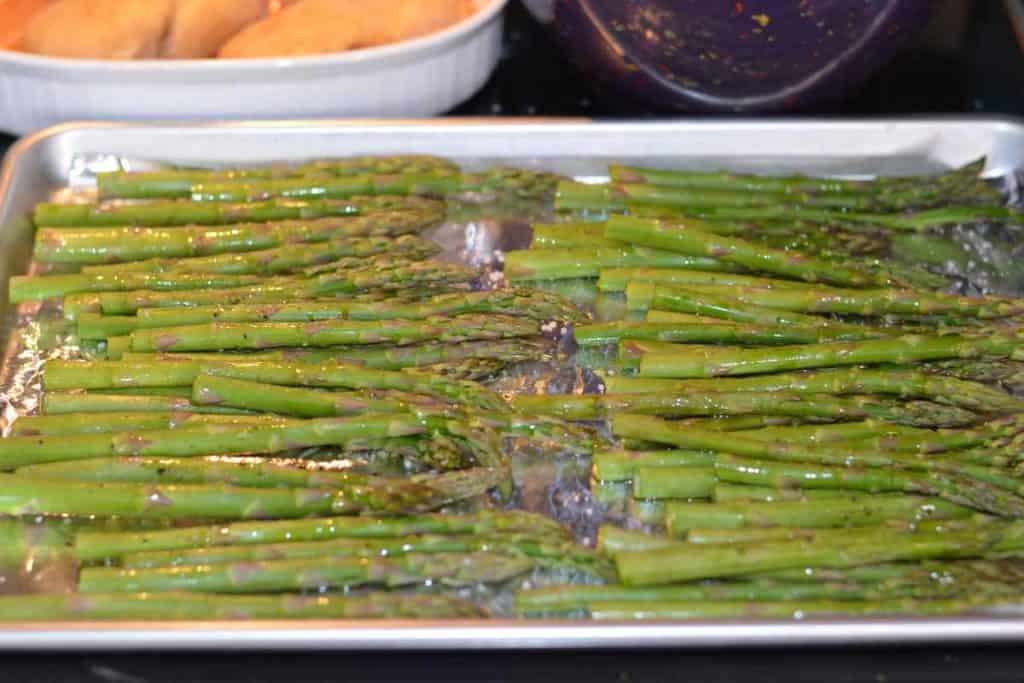 Asparagus with olive oil and salt and pepper lined up on a baking sheet, ready to go into the oven
