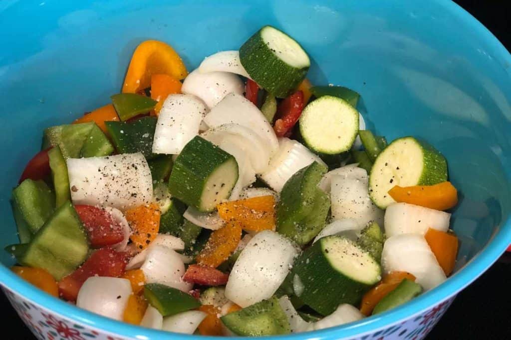 Salt and pepper sprinkled on a blue bowl of raw vegetables