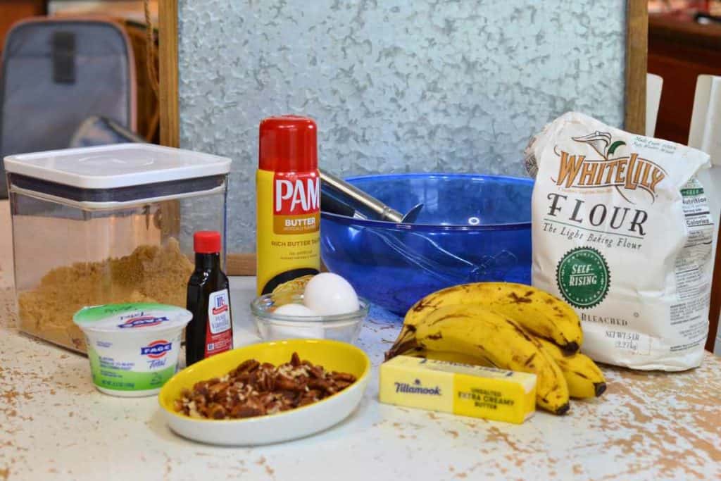 Ingredients for banana bread including self rising flour, bananas, butter, pecans, yogrut, vanilla, eggs, cooking spray and brown sugar