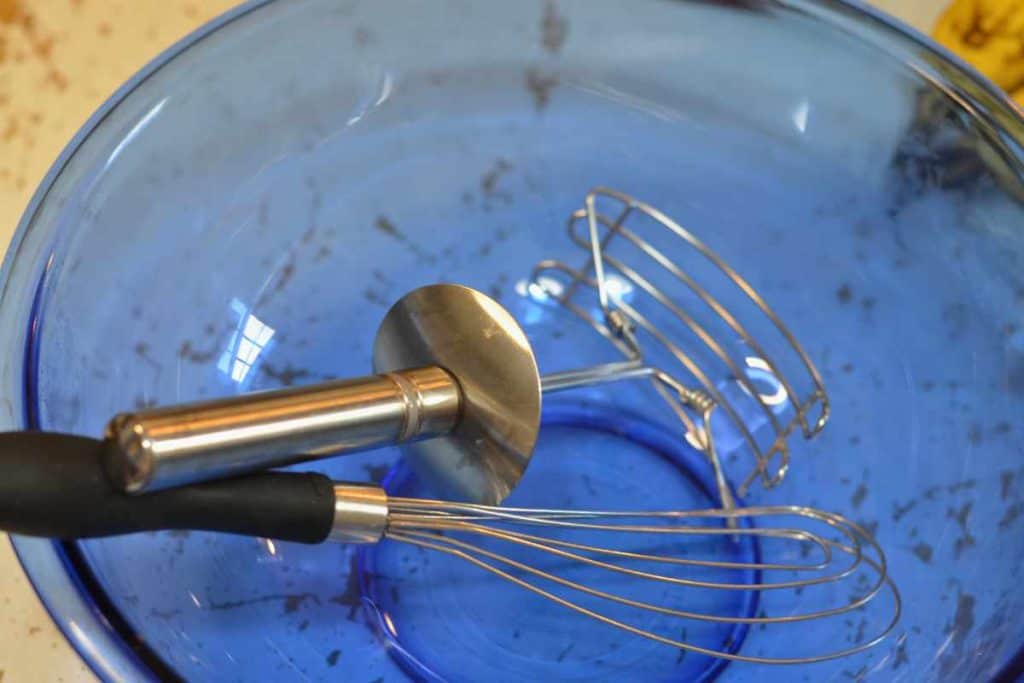 Pastry cutter and wire whisk in a blue glass bowl as equipment needed for banana bread recipe