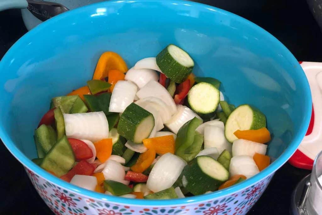 Chunky cut up vegetables including bell peppers, zuchinni, bell peppers and onions in a blue bowl