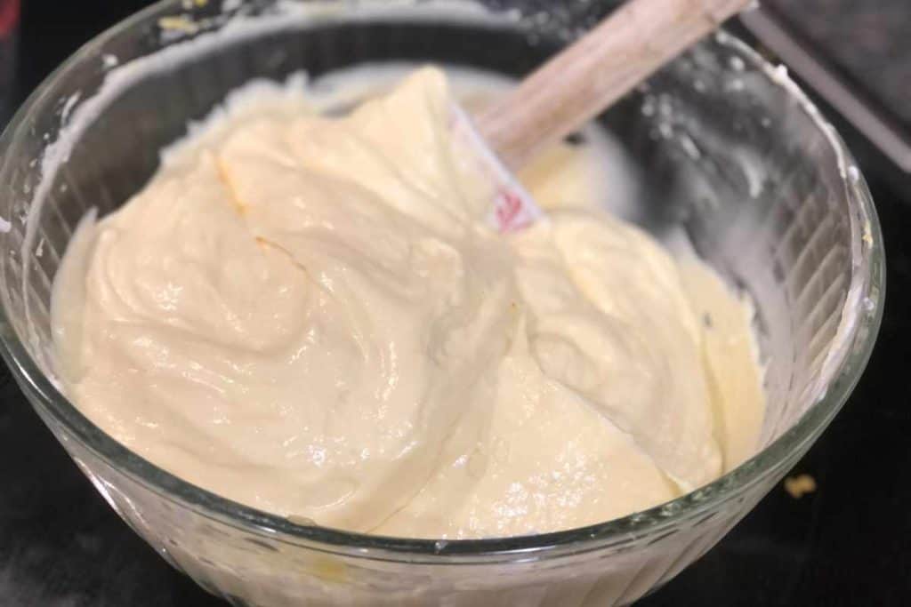 No bake lemonade cheesecake pie filling in a glass bowl being stirred by a spatula