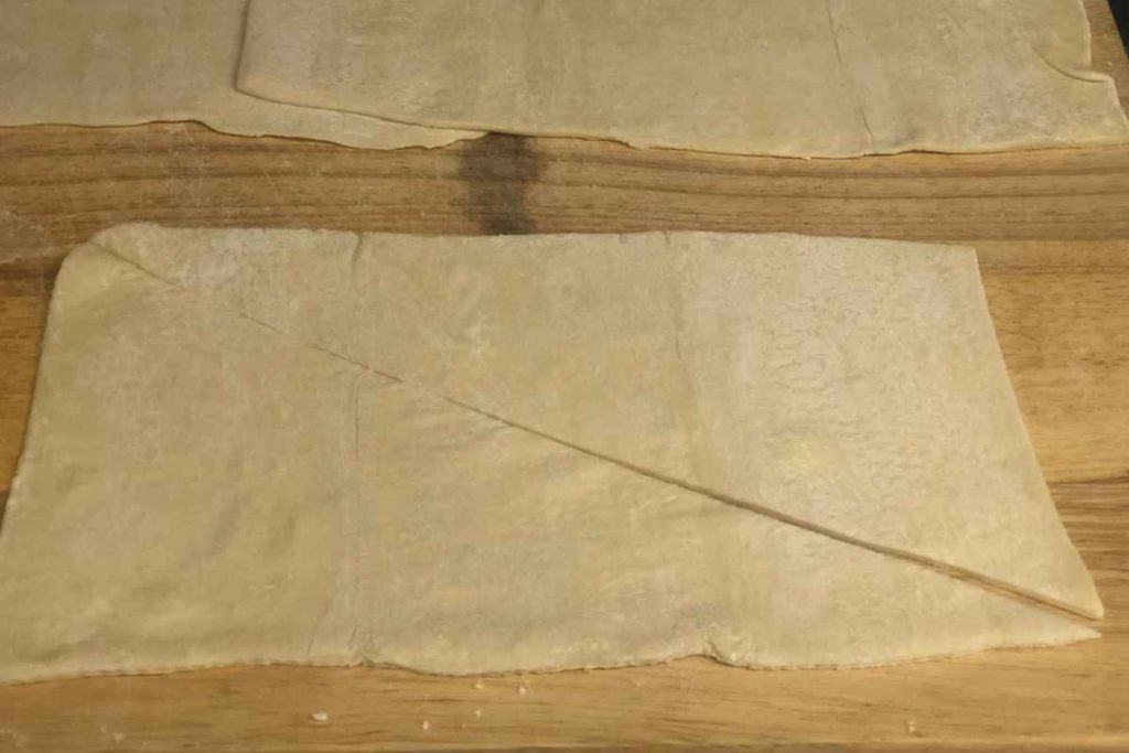 A rectangle of puff pastry cut into two triangles, ready to be used for almond croissants